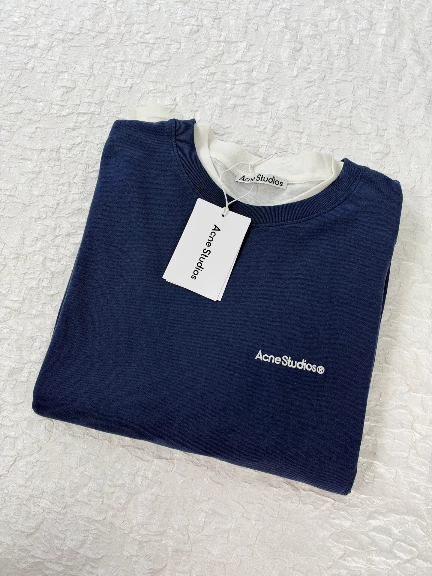 Acne Studio letter logo embroidered fake two-piece deconstructed long-sleeved T-shirt. Made of 100% cotton knitted plain fabric. The garment is pre-shrunk and washed to effectively reduce washing shrinkage. The version adopts dropped shoulder sleeves + loose box cut, the round neck is equipped with a rib collar, and the binding strip is used under the collar for reinforcement. The front chest uses high-density computer embroidery technology to present the brand logo. Visually, the inner and outer layers are designed with contrasting color splicing. The hem and cuffs are double-layered fake two-piece stacking. The sewing adopts flat seam + overlock technology. The lines are even and dense, and the overall relaxed silhouette takes into account practical wearability and layering effect. It can be worn alone or layered. Size：S/M/L/XL